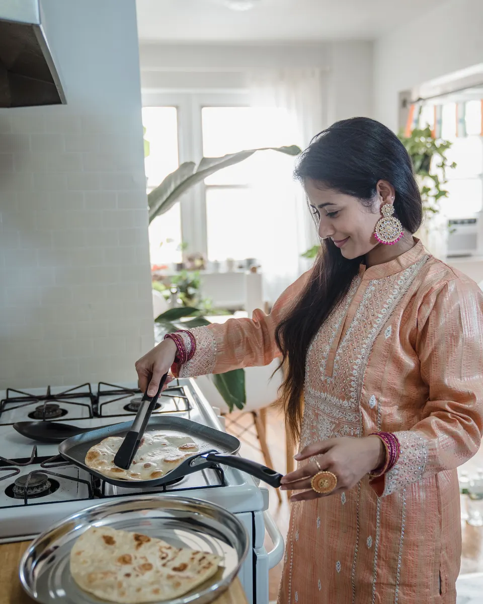 A woman in a kurta cooking flatbread at home
