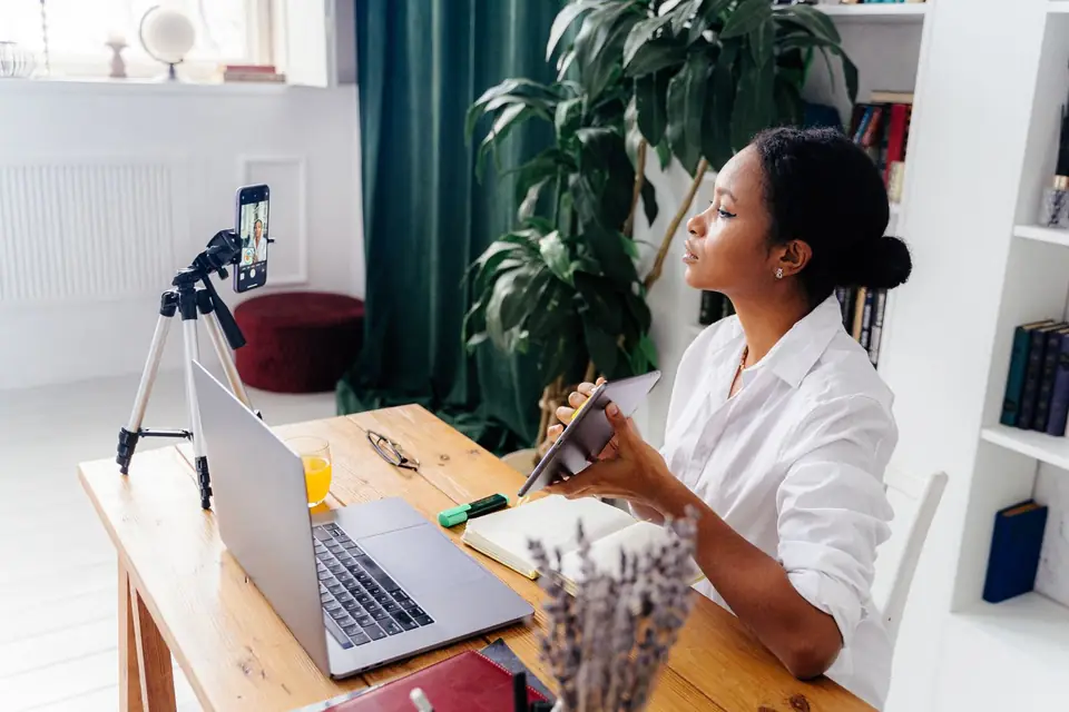 A young creator at her desk with a laptop and a phone on a tripod
