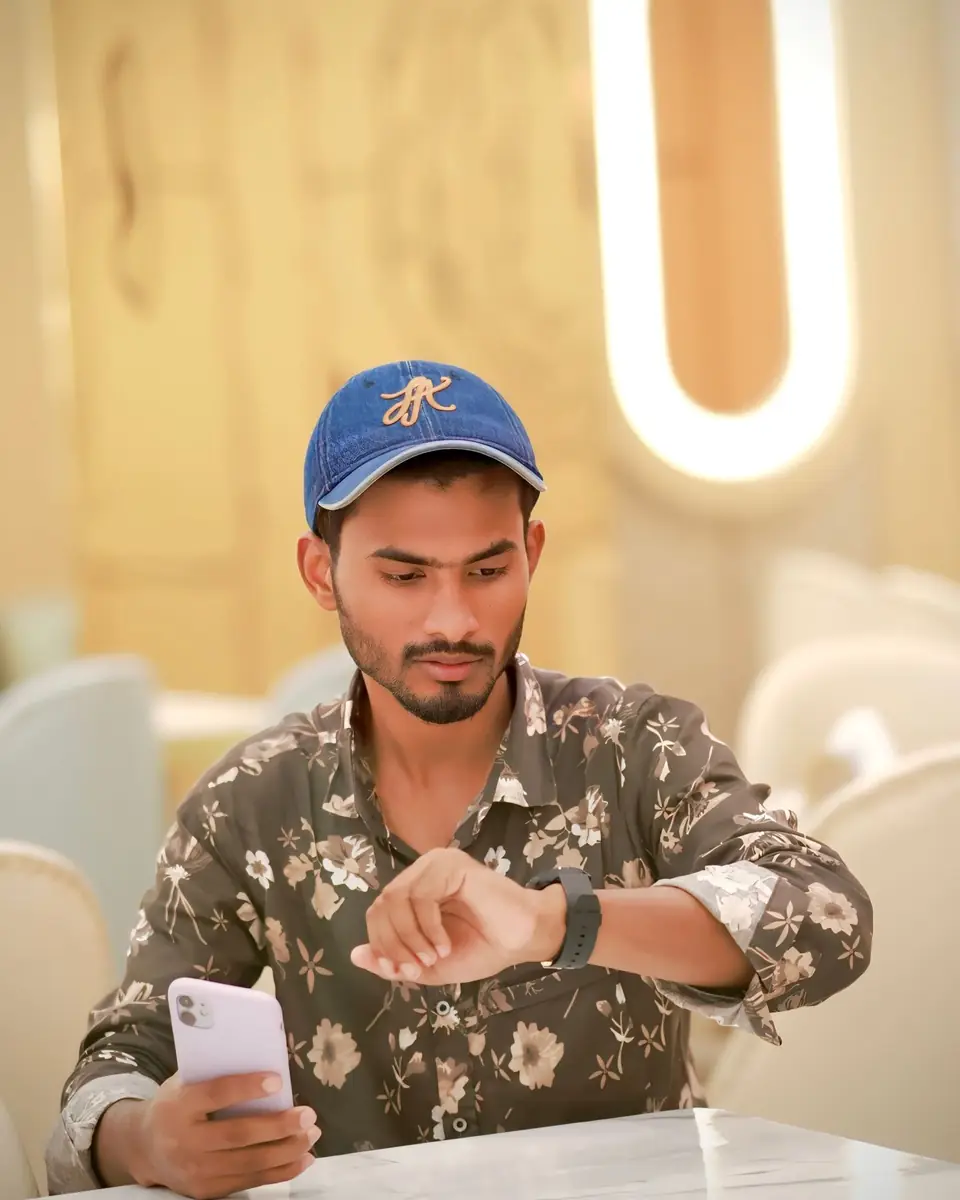 A young man checking his phone and watch at a café table