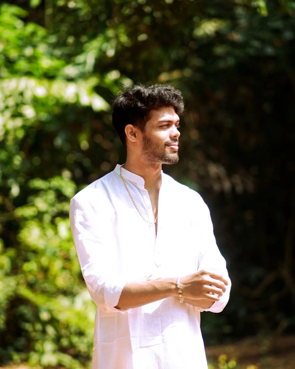 A young man in a white kurta standing in dappled sunlight