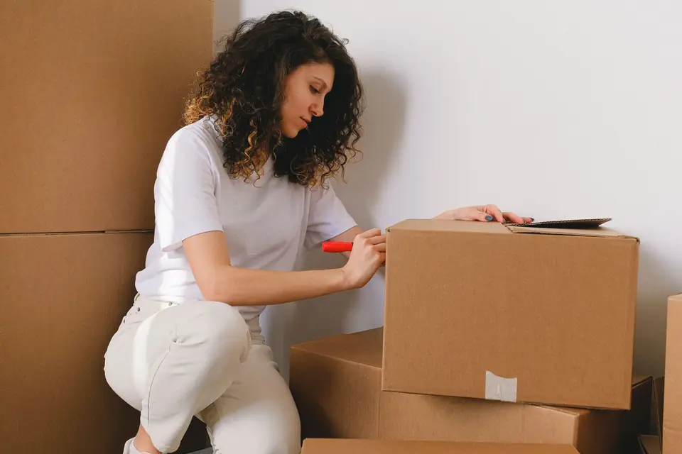 A woman writing on a cardboard box before it is shipped