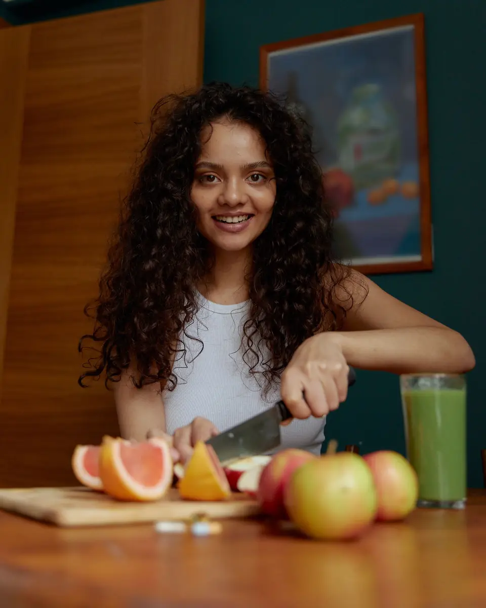 A young woman smiling as she slices fruit in her kitchen