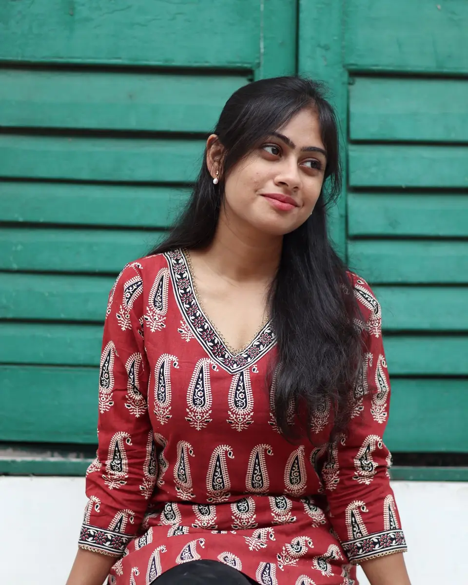 A young woman in a red kurta sitting against green shutters