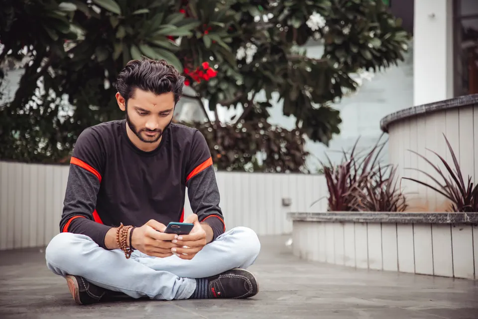 A young man sitting cross-legged and reading something on his phone