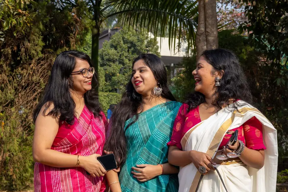 Three friends in sarees laughing together outdoors